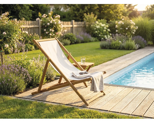 Sonnenstuhl aus Holz mit weißem Stoff auf einer Holzterrasse an einem Pool in einem Garten mit Lavendel und Rosen.