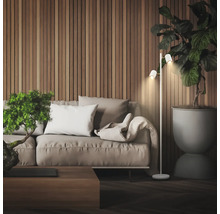Moderne Wohnzimmerszene mit einer zweiflammigen Stehleuchte neben einem Sofa vor einer Wand mit Holzlamellen und einer großen Zimmerpflanze.