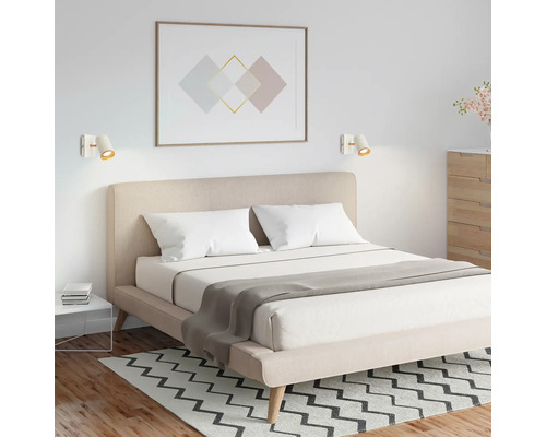 Modernes Schlafzimmer mit Doppelbett, beige gepolstertem Kopfteil und zwei weißen Wandstrahlern über dem Bett.