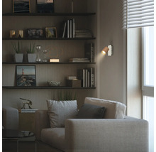 Moderne Wandleuchte mit Holzschirm in einem wohnlich eingerichteten Zimmer mit Sofa, Wandregalen und warmem Licht.