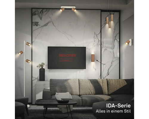 Helles, modernes Wohnzimmer mit Briloner Logo auf TV, IDA-Serie Leuchten an Marmorwand, Decke und als Stehlampe neben grauem Sofa.