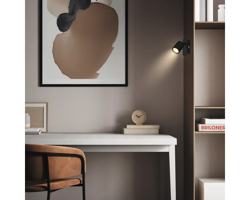 Schwarzer LED-Wandspot an einem Holzregal über einem hellen Schreibtisch in einem modern eingerichteten Arbeitszimmer.