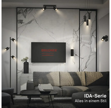 Modernes Wohnzimmer mit schwarzen Lampen der Briloner IDA-Serie, wie Stehleuchte, Wandleuchte und Pendelleuchte vor einer Marmorwand.