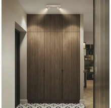 Moderner deckenhoher Einbauschrank in Holzoptik mit drei Türen und Deckenstrahlern in einem hellen Flur mit gemusterten Bodenfliesen.
