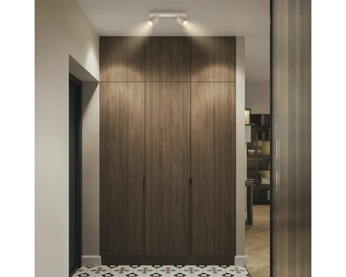 Moderner deckenhoher Einbauschrank in Holzoptik mit drei Türen und Deckenstrahlern in einem hellen Flur mit gemusterten Bodenfliesen.