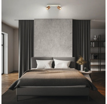 Moderner 2-flammiger Deckenstrahler in Holz-Optik über einem Doppelbett in einem minimalistisch eingerichteten Schlafzimmer.