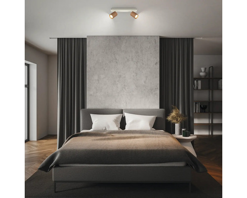 Moderner 2-flammiger Deckenstrahler in Holz-Optik über einem Doppelbett in einem minimalistisch eingerichteten Schlafzimmer.