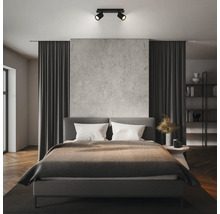 Moderner schwarzer Deckenstrahler zweiflammig in einem organisierten Schlafzimmer mit Betonwand und grauem Bett.