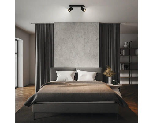 Moderner schwarzer Deckenstrahler zweiflammig in einem organisierten Schlafzimmer mit Betonwand und grauem Bett.