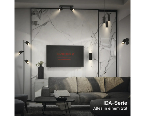Modernes Wohnzimmer mit schwarzen Lampen der Briloner IDA-Serie, wie Stehleuchte, Wandleuchte und Pendelleuchte vor einer Marmorwand.