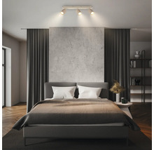 Moderner Deckenstrahler mit drei Spots in einem hellen, organisierten Schlafzimmer mit Doppelbett, Vorhängen und strukturierter Wand.
