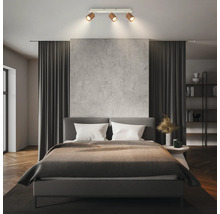 Dreiflammige Deckenleuchte mit verstellbaren Spots in einem modernen Schlafzimmer mit grauem Polsterbett und dunklen Vorhängen.