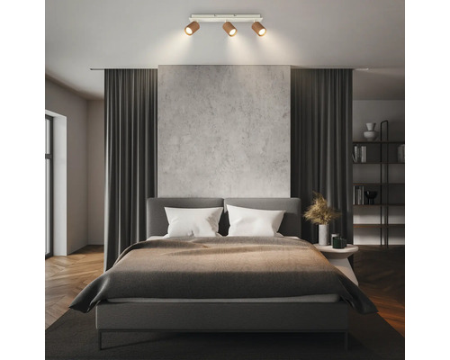 Dreiflammige Deckenleuchte mit verstellbaren Spots in einem modernen Schlafzimmer mit grauem Polsterbett und dunklen Vorhängen.