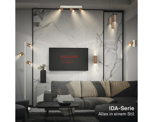 Wohnzimmer mit Lampen der Briloner IDA-Serie, darunter Deckenstrahler, Pendel-, Steh- und Wandleuchten vor einer Wand in Marmoroptik.