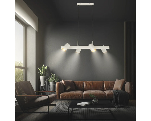 Weiße Pendelleuchte mit vier verstellbaren Strahlern in einem modernen Wohnzimmer mit braunem Ledersofa und dunklen Wänden.