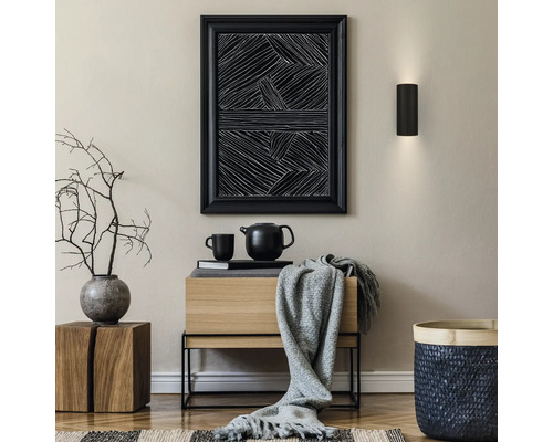 Moderner Innenraum mit schwarzer Wandleuchte, abstraktem Bild, Sideboard aus Holz, grauer Decke, Vase mit Zweigen und geflochtenem Korb.