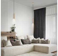 Modernes Wohnzimmer mit zwei zylindrischen Pendelleuchten über einem hellen Ecksofa mit vielen Kissen und dunklen Vorhängen.