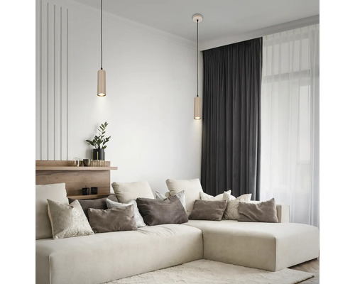 Modernes Wohnzimmer mit zwei zylindrischen Pendelleuchten über einem hellen Ecksofa mit vielen Kissen und dunklen Vorhängen.