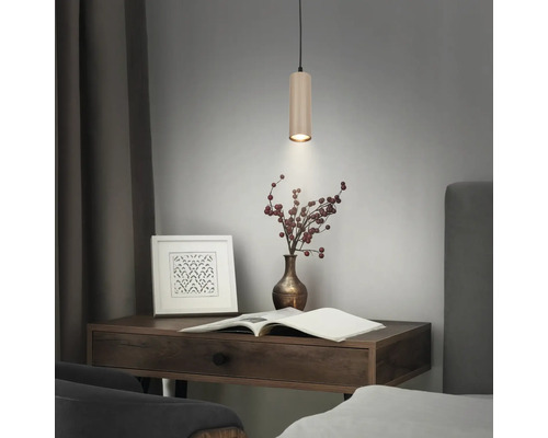 Moderne zylindrische Pendelleuchte mit gerippter Oberfläche in einer Wohnraumszene über einem Holzschreibtisch mit Dekorationsartikeln.