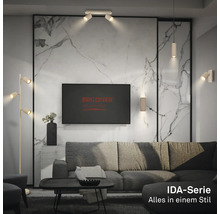 Modernes Wohnzimmer mit Deckenstrahlern, Wandlampen und Stehlampe der Briloner IDA-Serie sowie Briloner Logo auf dem Bildschirm.