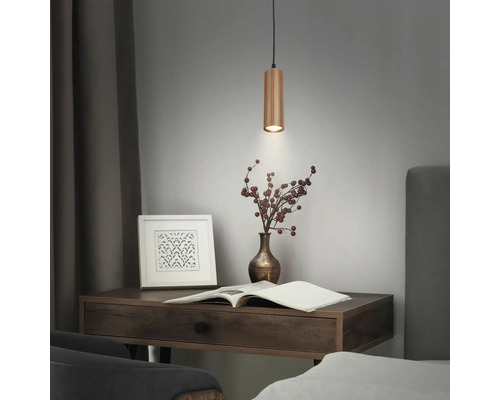 Zylindrische Pendelleuchte aus Holz über einem Schreibtisch mit Buch und Vase.