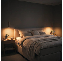 Modernes Schlafzimmer mit gepolstertem Bett, zwei Nachttischen aus Holz und tief hängenden Pendelleuchten mit warmem Licht.