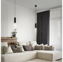 Zwei moderne schwarze zylindrische Pendelleuchten über einem beigen Ecksofa in einem hellen, aufgeräumten Wohnzimmer mit dunklen Vorhängen.
