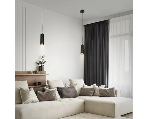 Zwei moderne schwarze zylindrische Pendelleuchten über einem beigen Ecksofa in einem hellen, aufgeräumten Wohnzimmer mit dunklen Vorhängen.