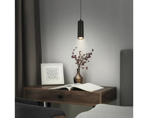 Moderne schwarze zylindrische Pendelleuchte mit gerippter Oberfläche über einem Schreibtisch aus Holz mit Buch und Vase.