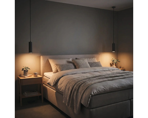Modernes Schlafzimmer mit gepolstertem Bett, grauen Kissen, zwei schwarzen zylindrischen Pendelleuchten und einem Nachttisch aus Holz.