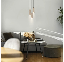 Modernes Wohnzimmer mit einer dreiflammigen zylindrischen Pendelleuchte über einem Couchtisch mit Schachspiel, grauem Sofa und grünem Hocker.