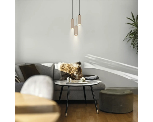 Modernes Wohnzimmer mit einer dreiflammigen zylindrischen Pendelleuchte über einem Couchtisch mit Schachspiel, grauem Sofa und grünem Hocker.