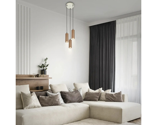 Dreiflammige Pendelleuchte mit zylindrischen Metallschirmen in einem hellen, modernen Wohnzimmer mit Ecksofa und dekorativen Kissen.