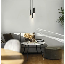 Drei schwarze zylindrische Pendelleuchten über einem modernen Wohnbereich mit grauem Sofa, rundem Couchtisch und einem Hocker.