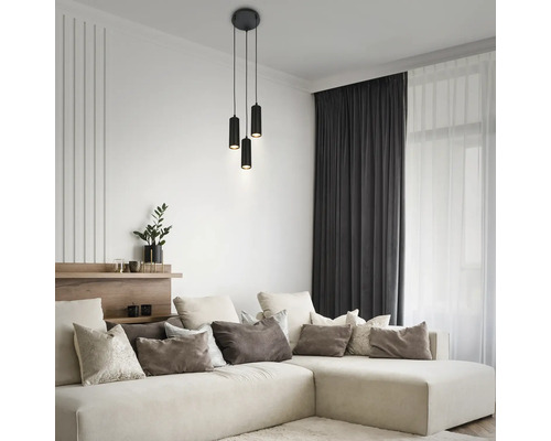 Modernes Wohnzimmer mit einer schwarzen dreiflammigen zylindrischen Pendelleuchte über einem großen beigen Ecksofa mit diversen Kissen.
