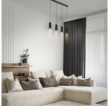 Modernes helles Wohnzimmer mit großem L-förmigem Sofa, Zierkissen, dunklen Vorhängen und schwarzer vierflammiger Pendelleuchte.