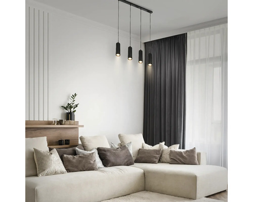 Modernes helles Wohnzimmer mit großem L-förmigem Sofa, Zierkissen, dunklen Vorhängen und schwarzer vierflammiger Pendelleuchte.