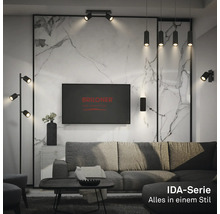 Modernes Wohnzimmer mit schwarzen Leuchten der IDA-Serie: Stehleuchte, Pendelleuchten und Spots. Marmoroptik-Wand, graues Sofa. Briloner Logo.
