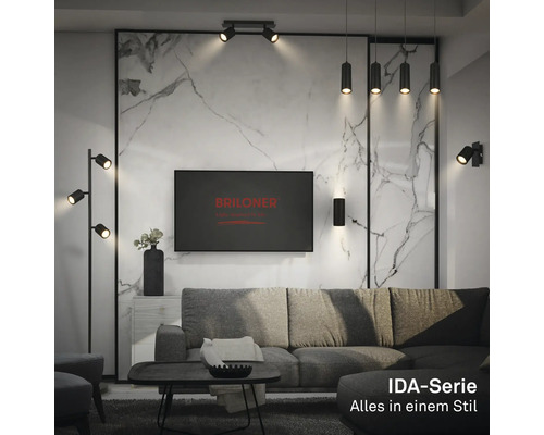 Modernes Wohnzimmer mit schwarzen Leuchten der IDA-Serie: Stehleuchte, Pendelleuchten und Spots. Marmoroptik-Wand, graues Sofa. Briloner Logo.