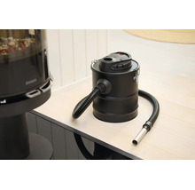 Elektrischer Aschesauger mit Metallbehälter und flexiblem Saugschlauch in einem hellen Raum neben einem Kamin.