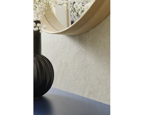 Nahaufnahme einer strukturierten Wand in Steinoptik mit einem runden Spiegel mit Holzrahmen und einer schwarzen Vase.