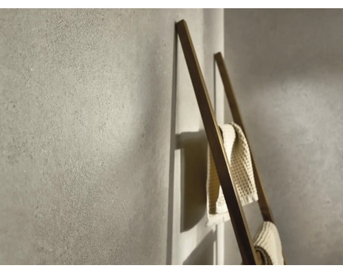 Strukturierte Wand in Steinoptik mit einer Handtuchleiter aus Holz und aufgehängten Handtüchern in einem modernen Badezimmer.