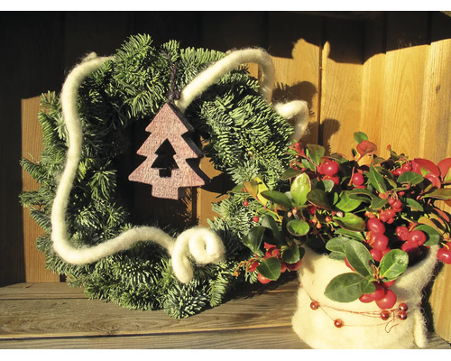 Weihnachtsdekoration mit Tannenkranz, Wollkordel, hölzernem Baum-Anhänger und Beerenpflanze in einer Wollumhüllung auf einer Holzoberfläche.