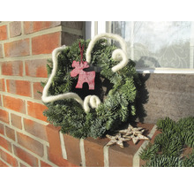 Weihnachtskranz aus echten Tannenzweigen mit weißem Wollband, Elchfigur aus Holz und Holzsternen auf einem Backsteinsims.