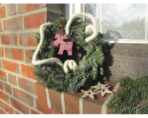 Weihnachtskranz aus echten Tannenzweigen mit weißem Wollband, Elchfigur aus Holz und Holzsternen auf einem Backsteinsims.