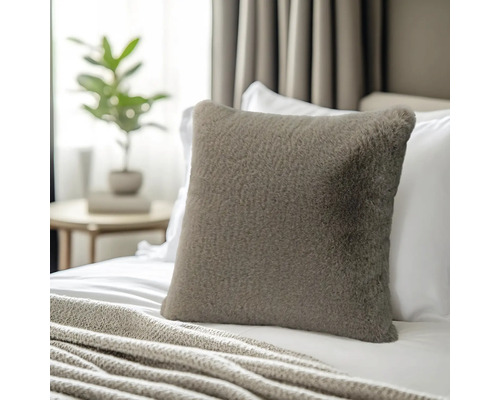 Quadratisches Dekokissen aus Kunstfell auf einem Bett mit Strickdecke in einem hellen Schlafzimmer.