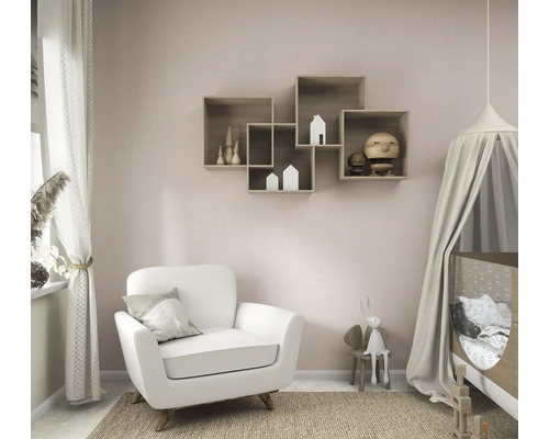 Helles, organisiertes Kinderzimmer mit weißem Sessel, Babybett inklusive Betthimmel und ineinandergreifenden Wandregalen aus Holz an einer rosa Wand.