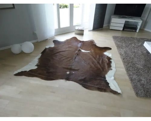 Naturgeformter Teppich aus Kuhfell in einem hellen, modern eingerichteten Wohnzimmer mit hellem Parkettboden.