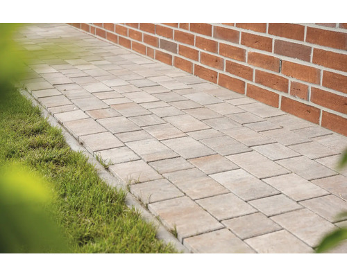 Gepflasterter Gartenweg aus rechteckigen Steinen zwischen einer Ziegelwand und einer Rasenfläche.