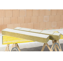 Mineralwolle-Dämmplatten mit weißer Beschichtung auf Arbeitsböcken vor einer Ziegelwand.